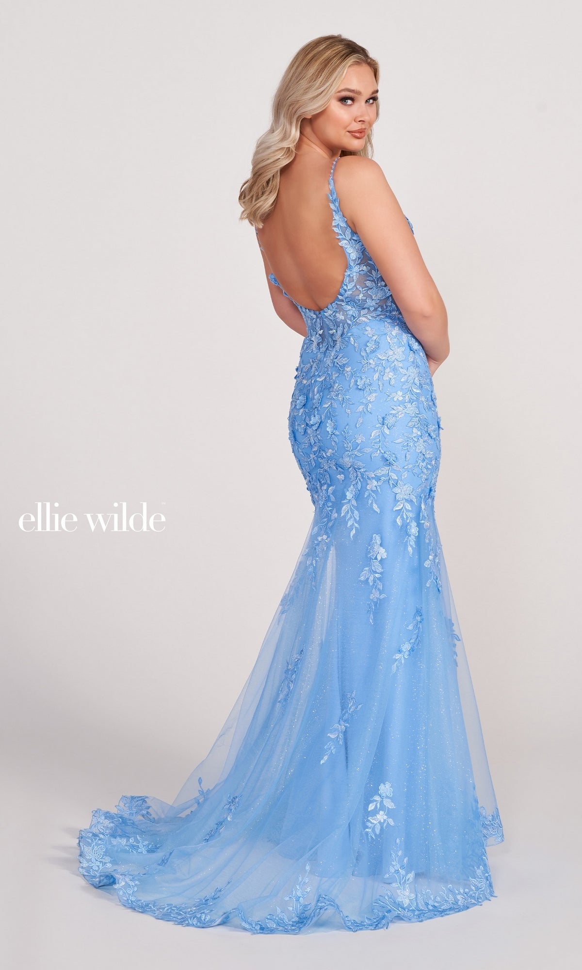 A woman stands gracefully, looking over her shoulder in a light blue Lace Embroidered Mermaid Gown With Sheer Bodice, featuring floral embellishments and delicate lace details.